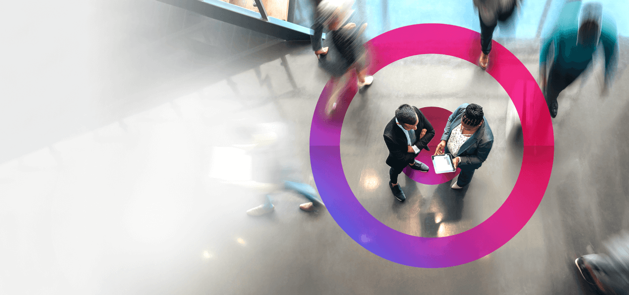 A male and a woman business figures wearing suits discussing project plans with a pink Cora lens circling them