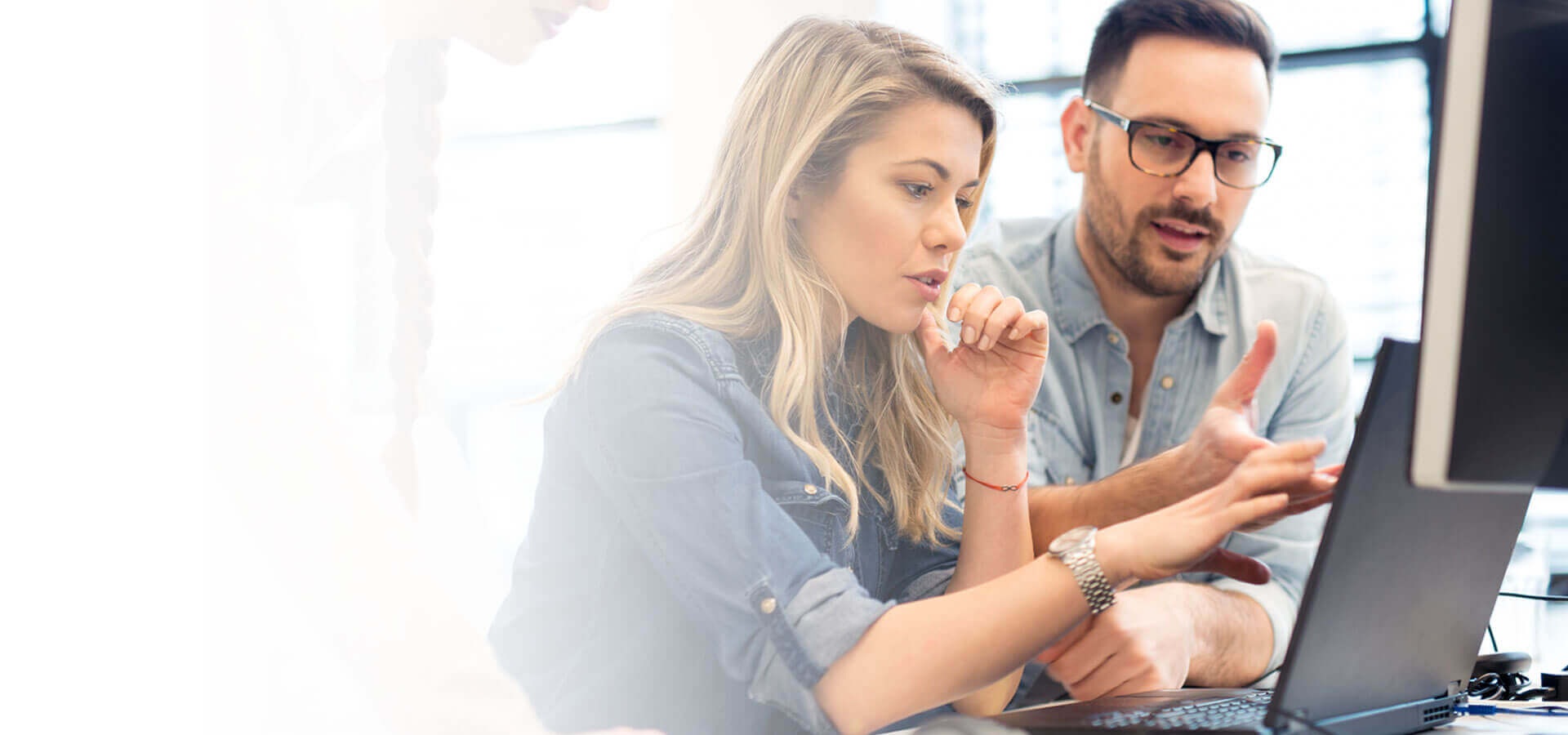 blonde woman and a brown haired man both wearing denim shirts explaining something on a laptop